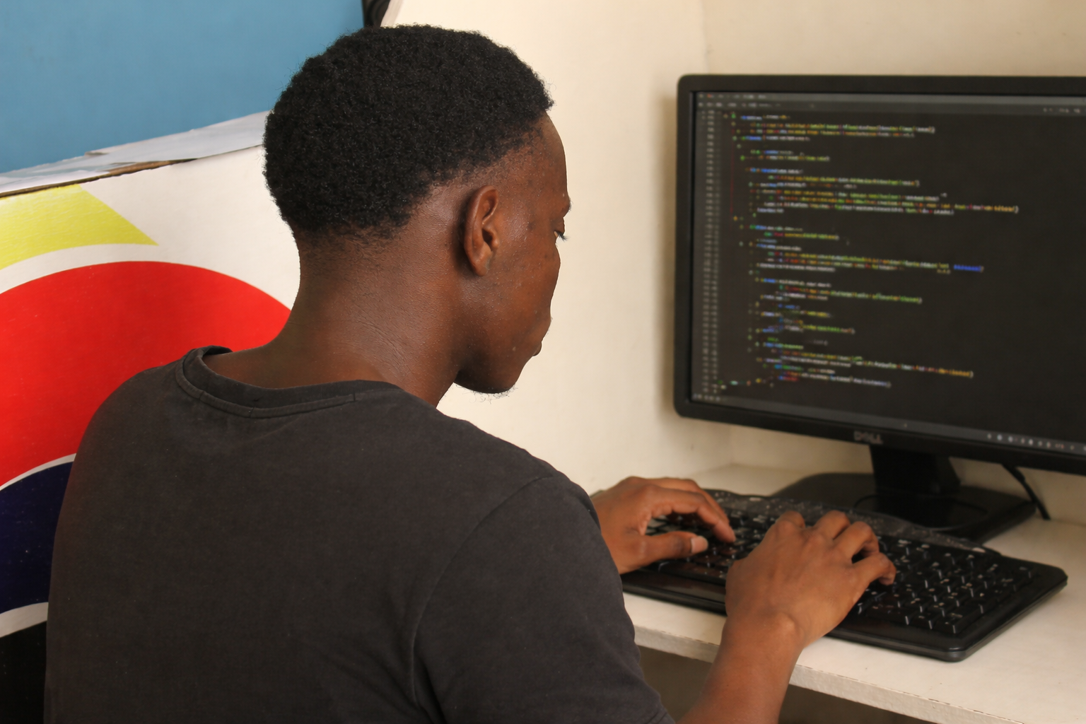 Fabiano Quirinda a programar no Cyber SM — sentado em frente ao computador, com código visível no ecrã, num dos primeiros dias de desenvolvimento do SaberAngola